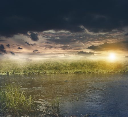 Graslandschaft mit Fluss bei Sonnenuntergang mit dunklen Wolke